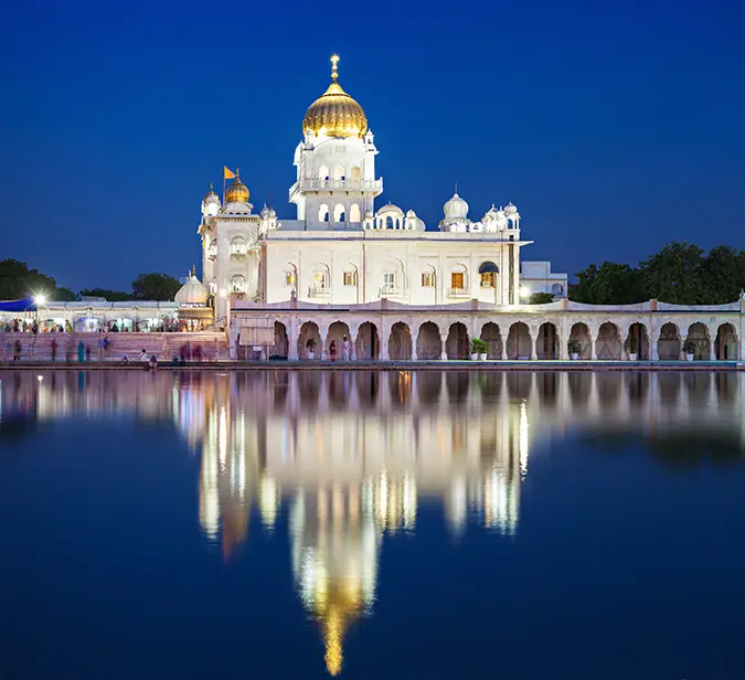 Sacred Sikh temple Bangla Sahib illuminated at night with reflection in holy pond in New Delhi.