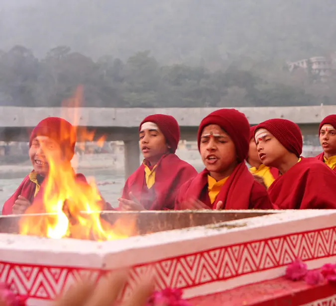 Spiritual ceremony with young monks performing fire rituals by Ganges river at sunset in Rishikesh.