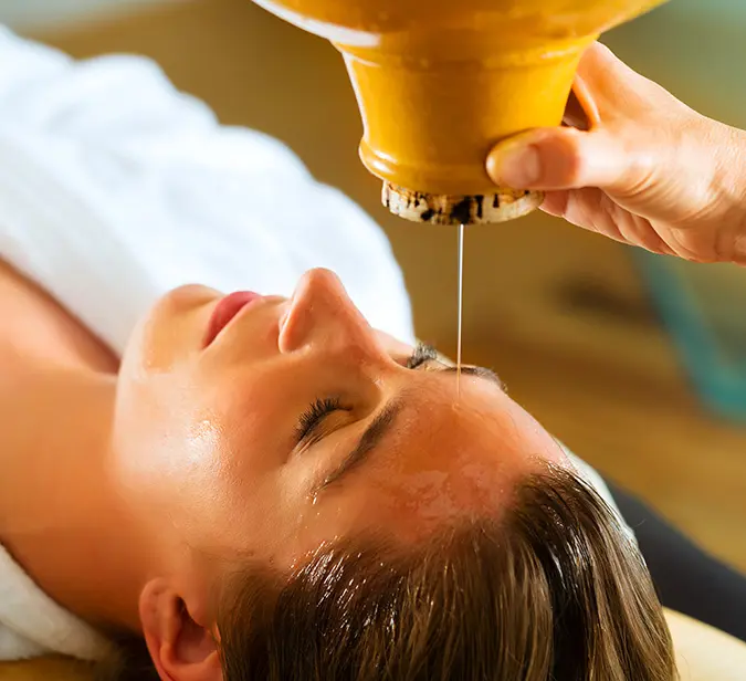 Warm oil drips on forehead during a calming Ayurveda treatment at Himalayan wellness retreat.