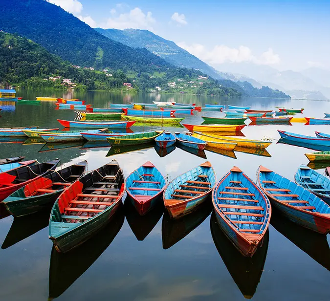 Colorful wooden boats floating on Pokhara’s serene Phewa Lake with Annapurna hills in background.
