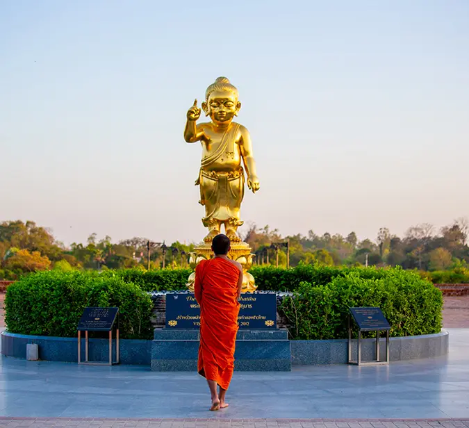 Buddhist monk walks toward golden statue of baby Buddha in sacred Lumbini garden.