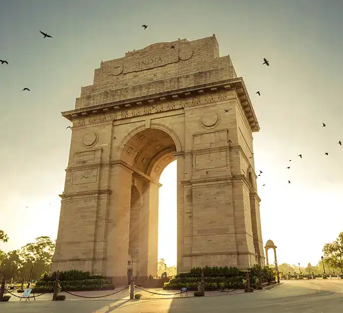 Historic India Gate with birds flying at sunrise, symbol of New Delhi’s colonial heritage.
