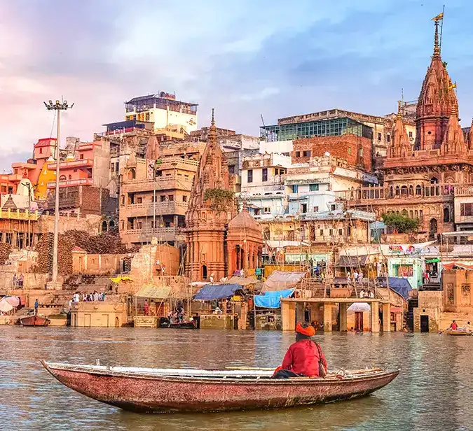 Traditional boat on Ganges River with historic Varanasi cityscape in the background.