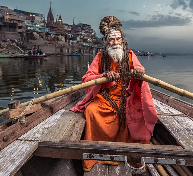 Traditional Indian sadhu navigating boat on Ganges at sunrise along the ancient ghats of Varanasi.