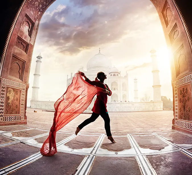 Silhouette of woman with flowing scarf in front of Taj Mahal during magical sunrise.