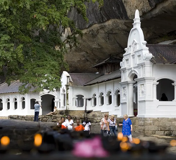 Exterior view of Dambulla Cave Temple with white arches and people walking around.