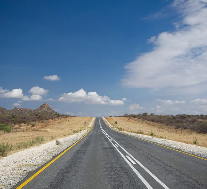 Scenic desert drive on a quiet Namibian highway beneath a vast, cloud-dappled sky.