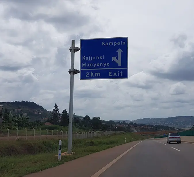 Road sign shows 2km exit for Kajjansi and Munyonyo, with Kampala straight ahead.