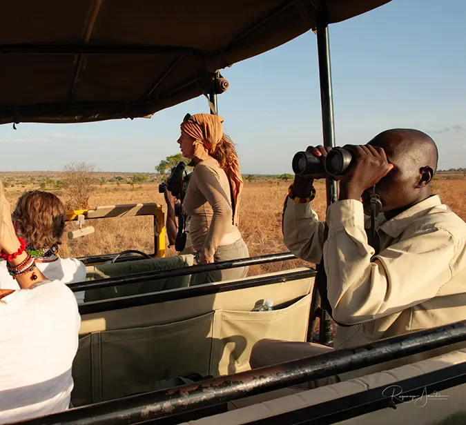 Visitors on game drive in Queen Elizabeth Park, viewing wildlife with guides and binoculars.