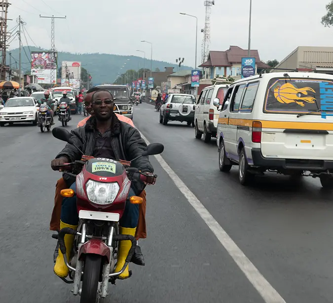 Motorbike rider navigates busy street near Congo-Rwanda border crossing.