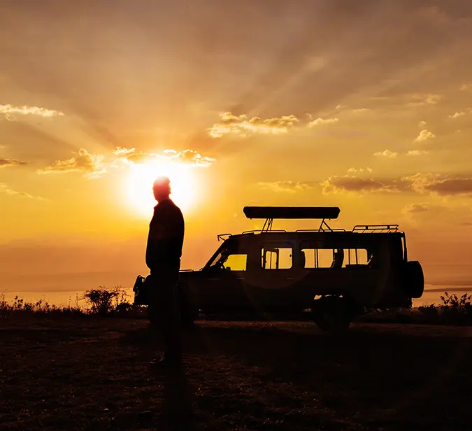 Traveller stands by safari jeep as the sun sets over the Rwandan highlands.