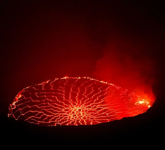 Bright red lava illuminating volcanic smoke in the darkness.