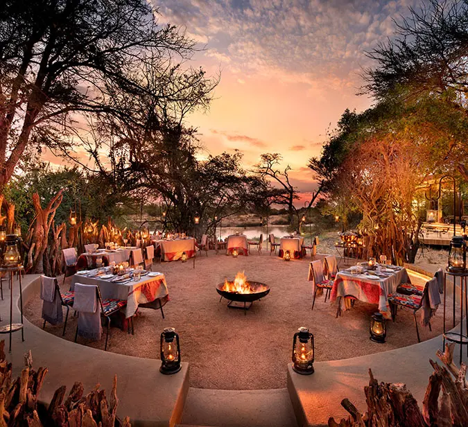 Magical bush dinner setup under lantern light in Serengeti with campfire and sunset views.