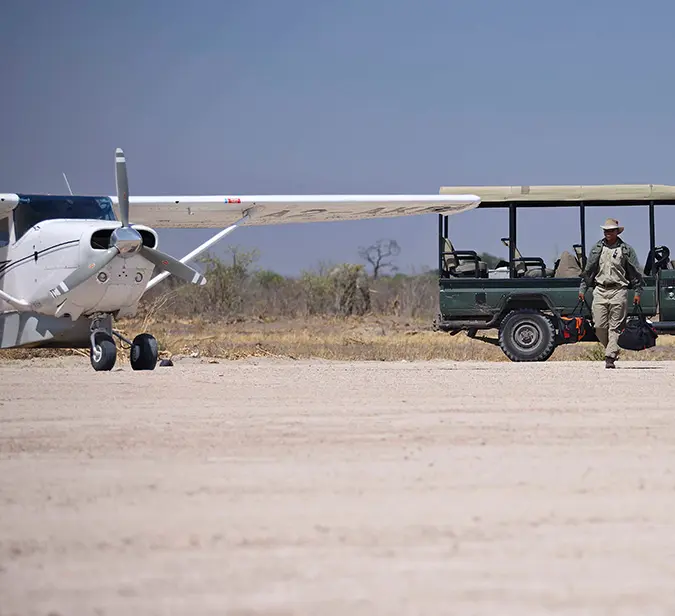 Safari arrival in Botswana with bush plane and open safari jeep at airstrip.