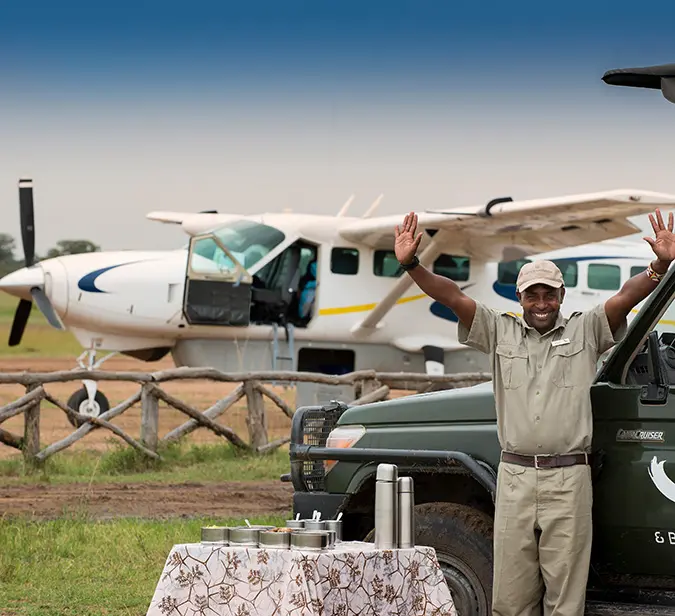 Guide waves beside safari jeep and bush plane before flight to Selinda Airstrip.
