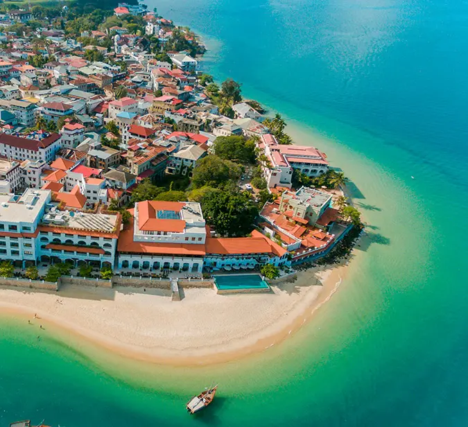 Aerial view of Stone Town Zanzibar with red-roofed buildings and turquoise coastline.