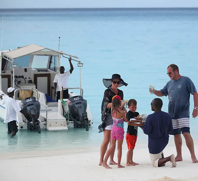 Family greeted with refreshments on Mnemba Island beach after scenic boat arrival.