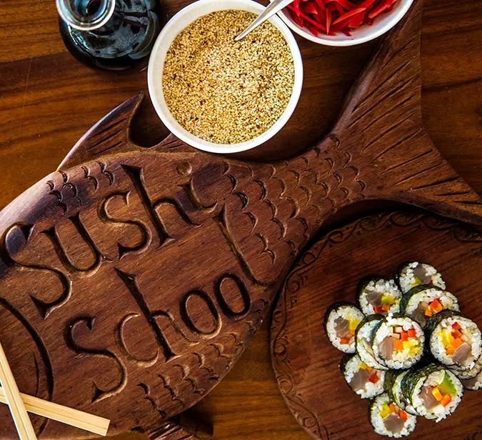 Handcrafted Sushi School board with sesame, pickled ginger, soy sauce, and sushi rolls.