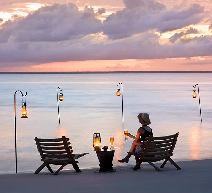 Sunset cocktail setup on the beach with lanterns and ocean view.