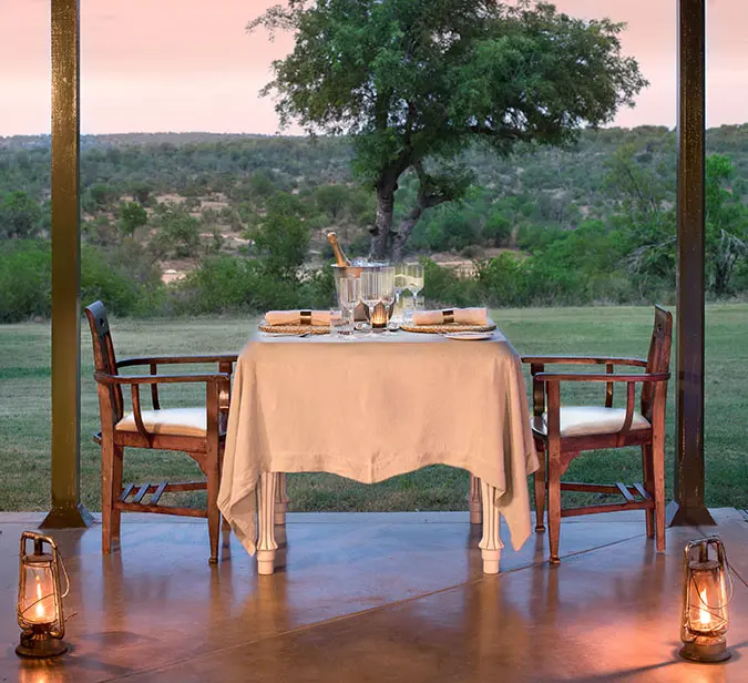 Elegant table for two overlooking African bushland at dusk.