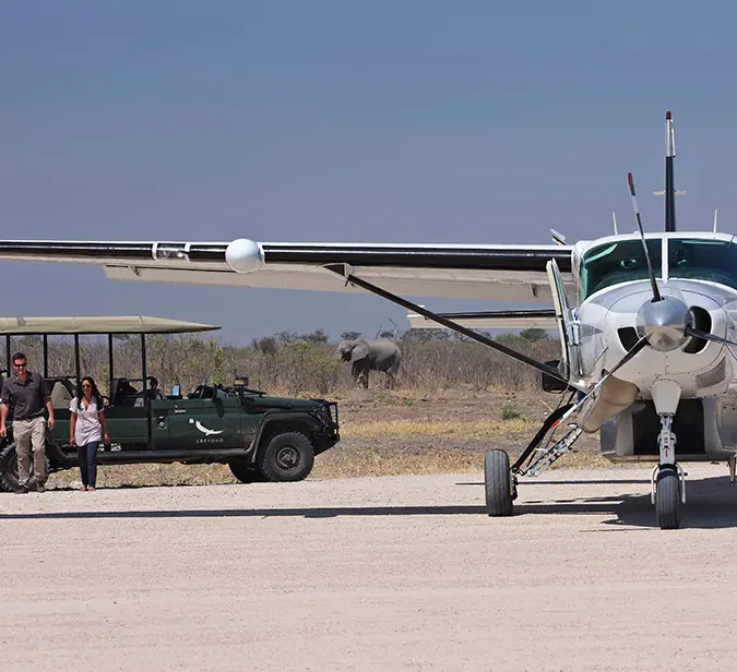 Light aircraft on remote airstrip at Mana Pools with safari jeep and elephant in the distance.
