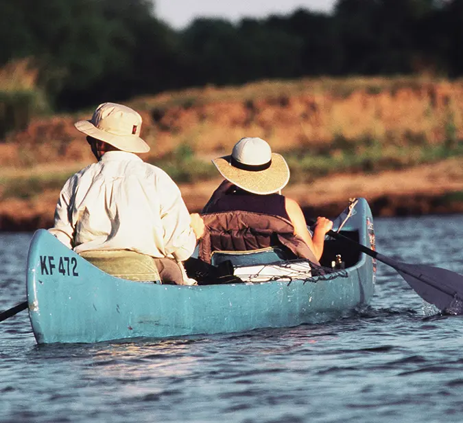 Two travellers in wide-brim hats canoeing on calm waters in Mana Pools National Park.