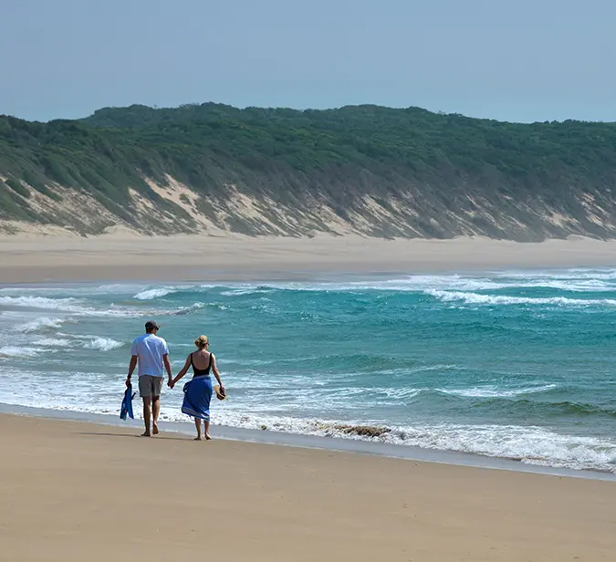 Couple walks barefoot along secluded beach near Dana Bay in South Africa.