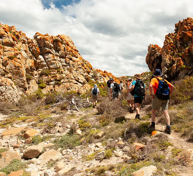 Group trekking through orange-hued rock formations on scenic hiking trail.