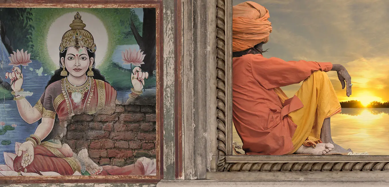Indian sadhu gazing at sunset by river beside ancient mural of Hindu Goddess Lakshmi.