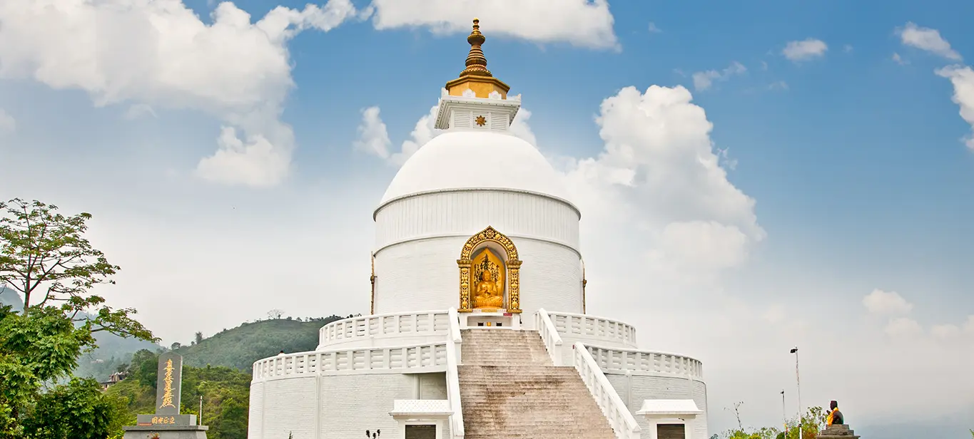 White Peace Pagoda stupa in Pokhara, Nepal surrounded by lush hills and blue skies.