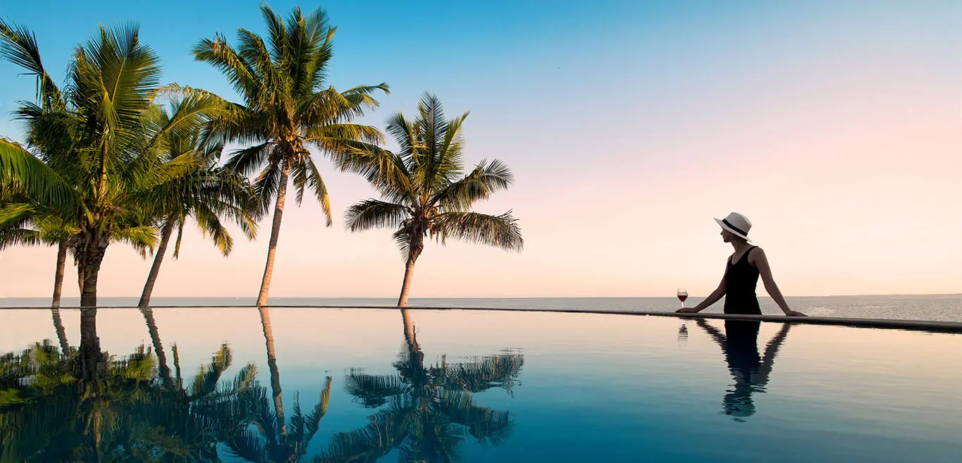 Sunset silhouette of woman enjoying wine in pool by the sea in Mozambique.